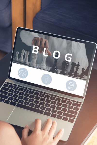 Hands typing on laptop displaying blog website and chess background